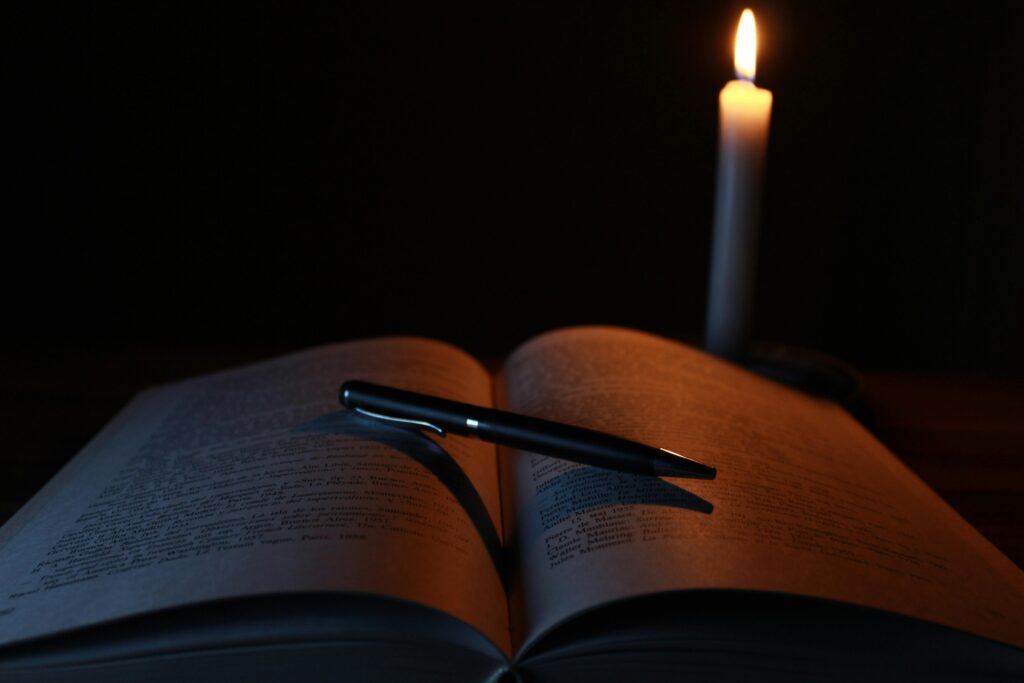 An open book and pen on a desk illuminated by candlelight, creating a tranquil study atmosphere.